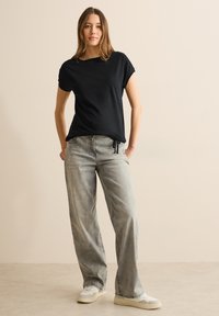 Sort kortærmet t-shirt med løs pasform, parret med lysegrå vidde jeans, stylet med hvide sneakers på en neutral baggrund.