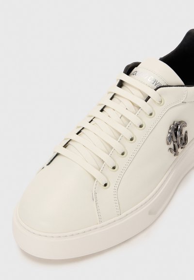 Vit lädersneaker med tjock sula, detaljerad silverorm-emblem på sidan, vita snörningar och svart inredning.
