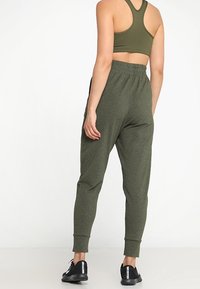 Olivově zelený sportovní outfit skládající se z přiléhavého crop topu a zúžených teplákových kalhot s elastickým páskem a manžetami na kotnících, doplněný černými teniskami.