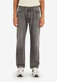 Jeans de mezclilla gris con un corte relajado, cinco bolsillos y costuras en contraste, combinados con zapatillas blancas y grises.