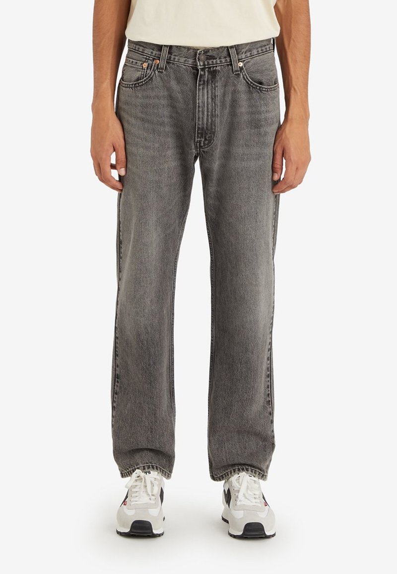 Jeans de mezclilla gris con un corte relajado, cinco bolsillos y costuras en contraste, combinados con zapatillas blancas y grises.