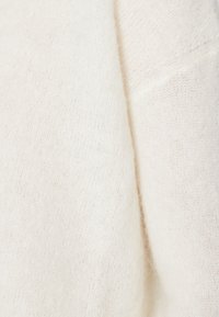 Světle béžový svetr s měkkým, texturovaným povrchem, s volným pletením a jemnými variacemi v hustotě nití.