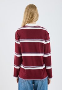 T-shirt à manches longues en bordeaux avec des rayures horizontales blanches et marines, présentant une coupe décontractée et un col rond, fabriqué en coton doux.