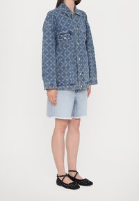 Kurtka dżinsowa z wzorem logo, niebieska, z dwoma kieszeniami na piersiach; noszona z jasnoniebieskimi szortami o postrzępionych brzegach oraz czarnymi balerinami z ćwiekami.