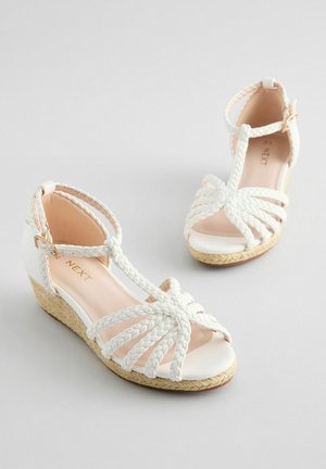 Vita klacksandaler med flätade remmar, öppen tå och ankelknäppning. Har en texturerad espadrille-inspirerad sula. Mjuk inre foder.
