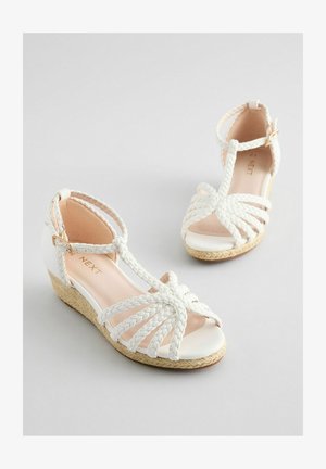 Sandalias de cuña blancas con tiras trenzadas, punta al aire y cierre en el tobillo. Presenta una suela texturizada inspirada en las espadrilles. Forro interior suave.