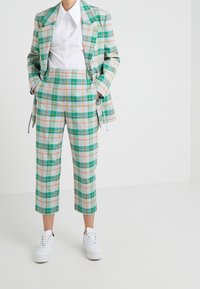 Kostium w kratę w odcieniach zieleni, niebieskiego i pomarańczowego; dopasowana marynarka z szerokimi klapami i skrócone spodnie; zestawione z białymi sneakersami i białą koszulą.