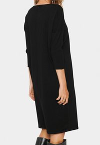 Abito nero oversize realizzato in tessuto a costine. Presenta un collo rotondo e maniche lunghe fino al gomito. L'orlo arriva poco sopra il ginocchio.