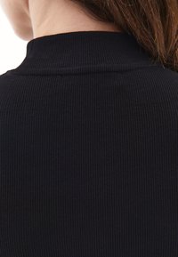 Czarny top z ryżowym materiałem charakteryzuje się wysokim dekoltem i subtelną teksturą, prezentując cienkie, pionowe linie i minimalistyczne wykończenia.