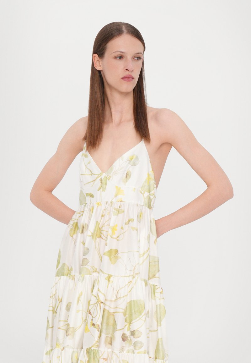 Vestido con estampado floral que presenta un fondo blanco con patrones de hojas verdes y amarillas, un escote en V y detalles de volantes en capas.