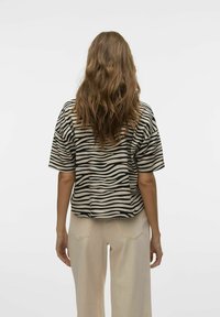 Haut à manches courtes rayé en zèbre beige et noir, présentant une coupe décontractée et une texture douce. Complété par un pantalon beige clair.