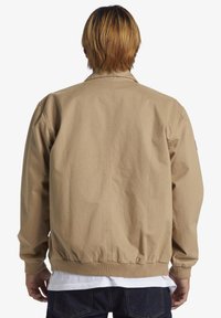 Beige bomber jacket with a relaxed fit, ribbed cuffs, and waistband; made from lightweight fabric with a smooth texture. No visible logos.