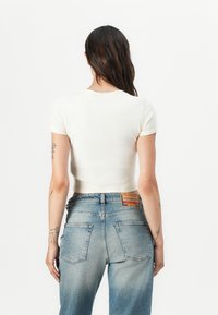 Short-sleeve, cropped t-shirt in pale yellow ribbed fabric, paired with high-waisted light blue denim jeans featuring a label on the back.