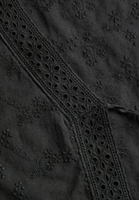 Tissu noir avec broderie florale et bande de dentelle décorative présentant des découpes ovales et circulaires en motif diagonal.