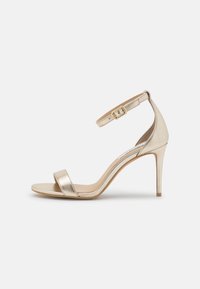 Kultaisesta metallista valmistetut korkokengät, joissa on kapea nilkkastrappi ja avokärkinen muotoilu. Kenkien pinnassa on sileä rakenne ja kapea korko.