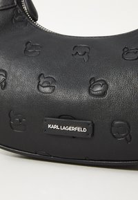 Borsa nera in pelle con motivi logo in rilievo, texture liscia, forma curvata e un'etichetta in tonalità argento con la scritta "KARL LAGERFELD."