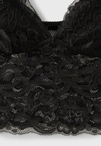 Bralette en dentelle noire avec motifs floraux et bords festonnés, avec bonnets souples et panneau en mesh au centre devant.