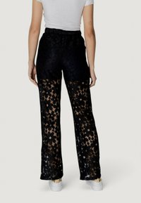 Pantaloni in pizzo nero con un motivo floreale e sezioni trasparenti. Vita elastica e vestibilità ampia, abbinati a sneaker bianche.