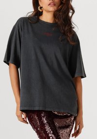 Zwart oversized T-shirt met korte mouwen en een ronde hals, voorzien van een klein rood grafisch ontwerp aan de voorkant. Gladde textuur.