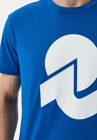 T-shirt in cotone blu con maniche corte caratterizzato da un grande logo grafico bianco, che include forme circolari e angolari.