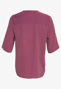 Krótki rękaw top w stonowanym kolorze mauve o gładkiej teksturze. Posiada prosty dół oraz detal w postaci karczka z tyłu. Brak widocznych detalów metalowych.