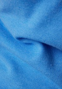 Hellblauer Stoff mit einem strukturierten, gewebten Muster. Das Material wirkt weich und biegsam und zeigt subtile Variationen im Farbton.