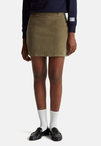Olivově zelená midi sukně z kordu s texturovaným povrchem, předními kapsami a přiléhavým střihem. Spojena s černými mokasíny a bílými ponožkami.