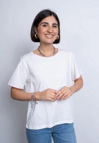 Maglietta di cotone bianca con maniche corte, caratterizzata da accenti rossi sul collo e sulle maniche. Abbinata a jeans blu e braccialetti colorati.