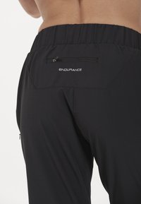 Svarta träningbyxor med elastisk midja, utrustade med en liten zip-ficka och märket "ENDURANCE" tryckt på baksidan.
