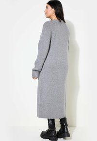 Long gilet gris ajusté en matériau tricot doux, avec des poignets côtelés et un ourlet droit. Associé à des bottes noires lourdes à lacets.