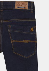 Jeans de mezclilla azul oscuro con costuras naranjas, que presentan una etiqueta de cuero en la cintura y un diseño de bolsillo único en la parte trasera.