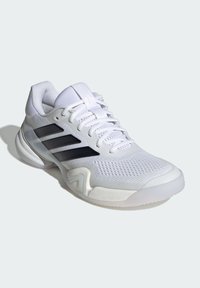 Biela športová obuv s textilným zvrškom zo sieťoviny, tromi čiernymi pruhmi, polstrovaným golierom a textúrovanou gumovou podrážkou. Má odpruženú medzipodrážku pre podporu.