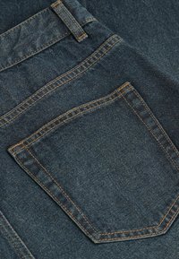 Jeans de mezclilla azul oscuro con costuras naranjas en contraste, que cuentan con un bolsillo trasero y un acabado texturizado. Corte clásico con una cinturilla estándar.