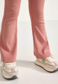 Bredde lyserøde ribbede bukser parret med klodsede beige sneakers med pastelfarver og en sort sål.