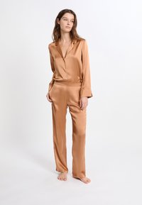 Satin-Schlafset in warmem Bronze, bestehend aus einem Hemd mit Kragen und Knöpfen sowie einer locker sitzenden Hose mit elastischem Bund. Glatte Textur.