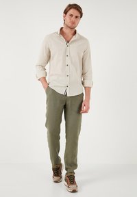 Camisa de manga larga beige con botones negros, combinada con pantalones verde oliva y zapatillas beige-marrón con un patrón de camuflaje.