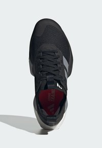 Sort atletisk sko med en tekstureret overdel, grå detaljer og en rød indersål. Har snørebånd og en polstret sål for støtte.