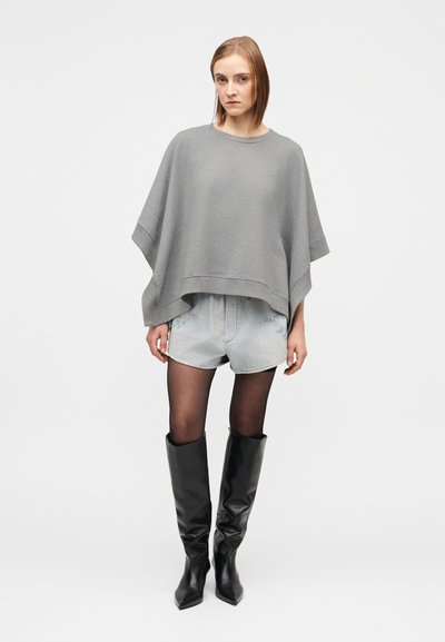 Sivi ohlapen pulover z znižanimi rokavi, kombiniran z jeans kratkimi hlačami. Model nosi črne usnjene škornje nad koleni in prozorne črne nogavice.