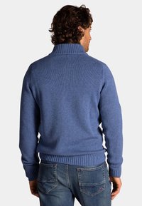 Blauwe gebreide trui met een hoge kraag, geribde manchetten en zoom. Gedragen over denim jeans, die een gestructureerde stof en een getailleerd ontwerp tonen.