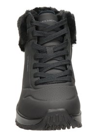 Botte d'hiver noire avec un extérieur en cuir lisse, un col en fourrure et une semelle en caoutchouc texturé. Présente des lacets noirs et des détails perforés.