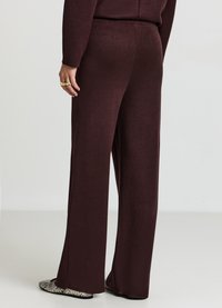 Pantaloni bordeaux a gamba larga con una texture liscia, vita elastica e cucitura laterale discreta. Indossati con scarpe piatte con motivo.