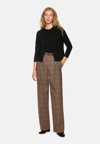 Schwarze Strickjacke mit drei Viertelärmeln, Knopfverschluss, kombiniert mit hochgeschnittenen Karohosen in Beige, Rot und Grün.