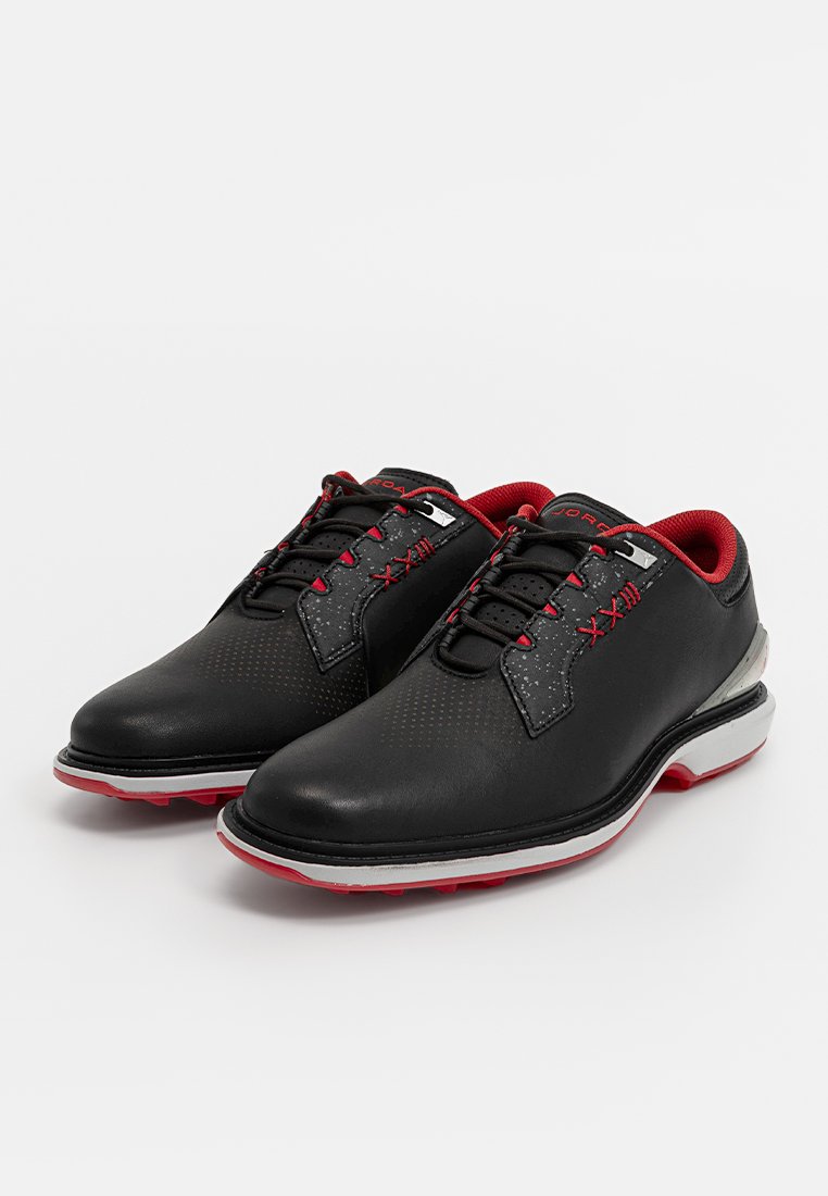 Chaussures de golf noires avec des accents rouges, dotées d'un cuir lisse, d'un design perforé, d'un logo circulaire et d'une semelle rembourrée pour le confort.