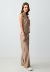 Beige gestreepte pak met een mouwloos vest met knoopdetails en bijpassende wijde broek, gecombineerd met witte sneakers.
