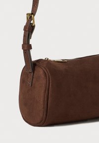 Borsa in suede marrone con forma arrotondata, tracolla regolabile e hardware in tonalità oro. Presenta una chiusura a zip lungo il bordo superiore.