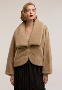 Giacca beige in pelliccia sintetica con ampio colletto, design corto e consistenza morbida. Presenta un orlo arrotondato e maniche a vestibilità rilassata.