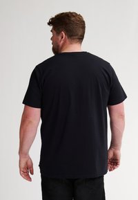Camiseta de algodón negra con cuello redondo y mangas cortas, que presenta un diseño liso y un corte relajado. Detalle de costura visible en el dobladillo.