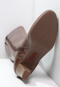 Brun läderankelboots med en sid زيبر, slät textur, låg klack och en mönstrad gummisula med en märkesinlägg.