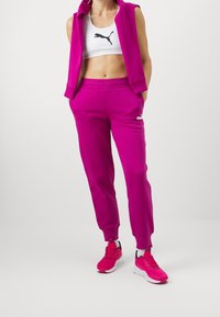 Fuksjowy dres z bezrękawnikem i spodniami dresowymi. Biały stanik sportowy z czarnym logo. Jasnoróżowe buty sportowe z czarnymi akcentami.