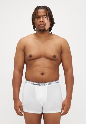 Boxeri din bumbac alb cu o talie neagră "POLO RALPH LAUREN", având o croială strânsă și o textură netedă. Modelul stă în picioare.